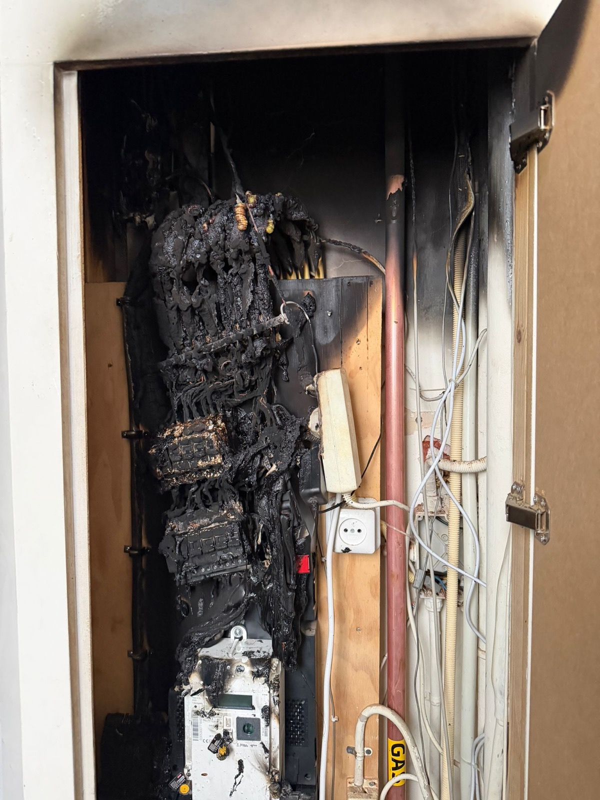 Volledig verkoolde groepenkast in een meterkast; de bedrading hangt in gesmolten slierten over de verbrande meter